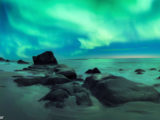 Panoramic view of Northern Lights aurora borealis dancing over rocky beach in Lofoten Norway